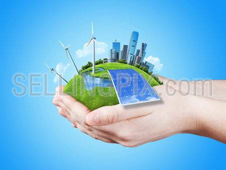 Hands holding clear green meadow with sun battery block, wind mill turbines and city skyscrapers. Concept for ecology, growing business, freshness, freedom. Green fields collection.